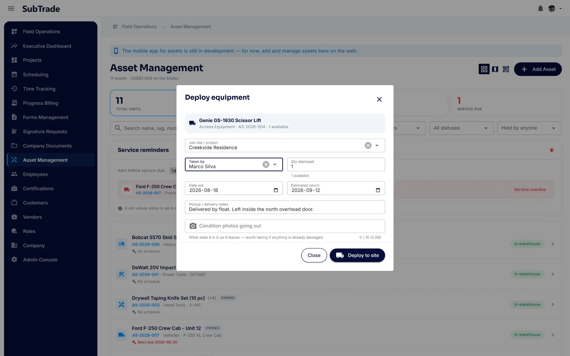 The Deploy equipment dialog in SubTrade assigning a scissor lift to a job site and a named crew member, with quantity, date out, estimated return, delivery notes and condition photos